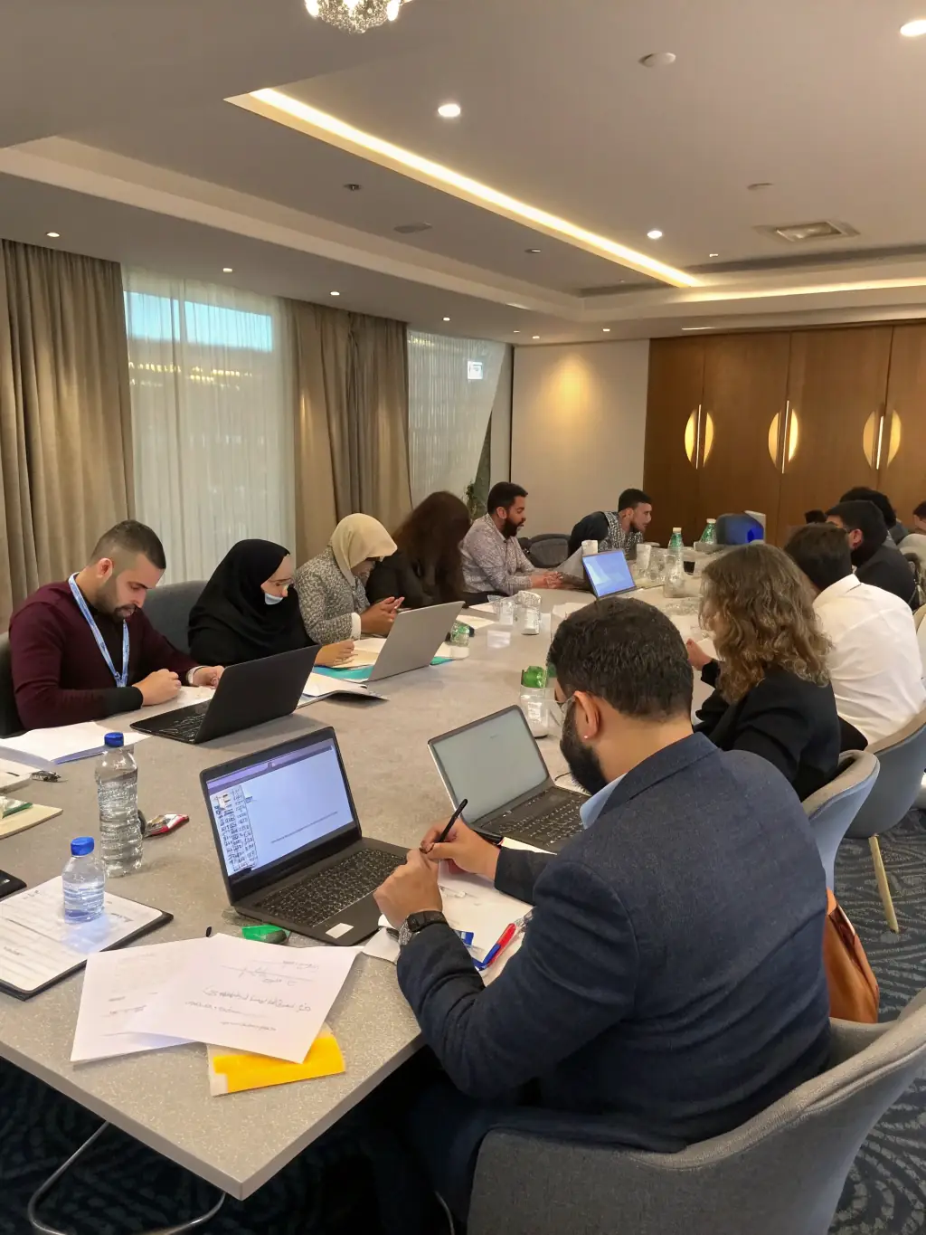 A diverse group of professionals is participating in a hands-on training session, using laptops and interactive whiteboards to learn about digital tools and cybersecurity best practices.